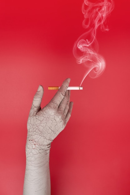 Dry and cracked hand holding a smoking cigarette, bad effects of smoking on skin.