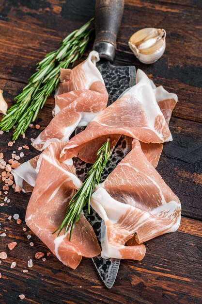 Dry cured Prosciutto crudo parma ham on a butcher knife. Dark wooden background. Top View.