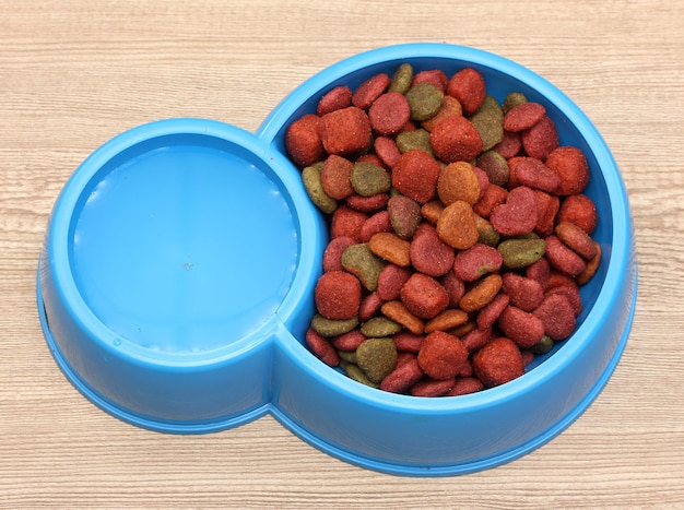 Dry dog food and water in blue bowl on wooden background