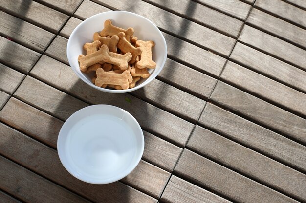 Dry dog food and water in bowl on wooden background top view.