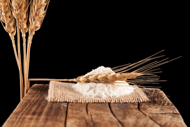 Dry ear of wheat or rye and pile of flour on vintage cutting board.