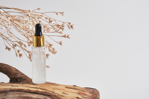 Dry flowers, bottle with a pipette with gel serum on a wooden log on a gray background, mock-up background for your product presentation, naturally organic cosmetics or product concept