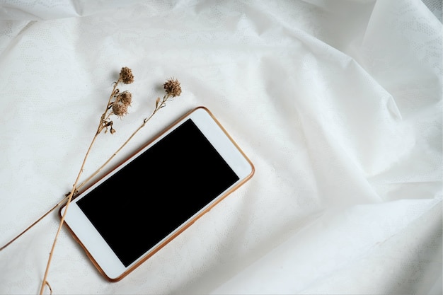 Photo dry flowers and smartphone on white tablecloth