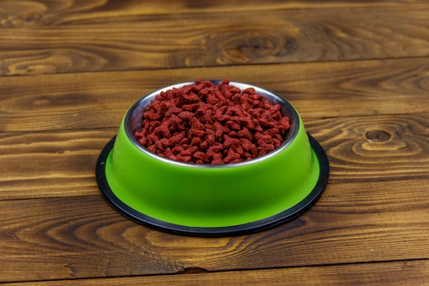 나무 배경에 있는 그릇에 있는 고양이나 개를 위한 건조 식품 목재 표면에 있는 애완동물 사료