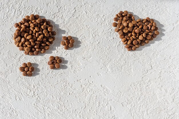 Dry food for dogs and cats in the shape of a heart and in the shape of a footprint on a white plaster background, copy space, top view. The concept of love for pets. Healthy pet food concept