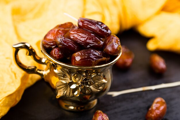 Dry fruit dates in golden cup near slate black heart.