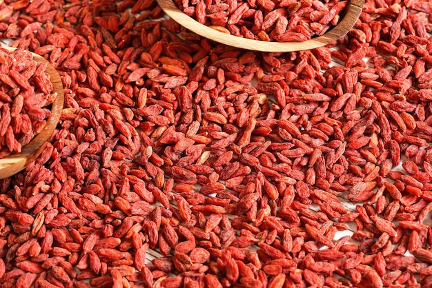 Dry goji berries in small wooden bowls, scattered on desk below