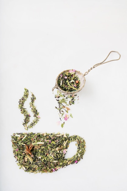 Dry herbal tea leaves in shape of cup with smoke and a strainer over the cup on white background