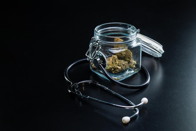 Dry medical cannabis in a jar with a stethoscope on a black background