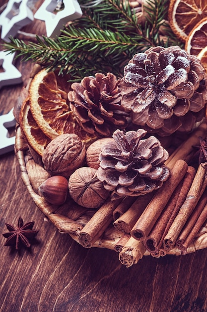 Foto arancia secca, anice stellato, cannella, pigne e abete in piatto rustico su tavola di legno. idea medley fatta in casa per l'atmosfera e l'aroma natalizio. natale ecologico con decorazioni naturali fatte in casa.