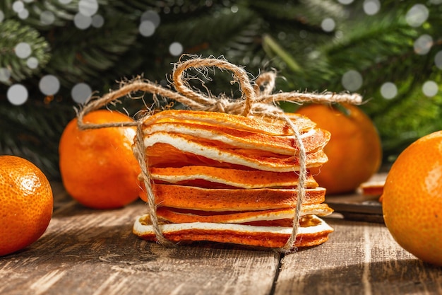 Dry oranges slices snack. Dried citrus fruits for Christmas decorations. Tangerines with leaves, fir tree branches, scissors, and thread. Wooden background, rustic concept, close up