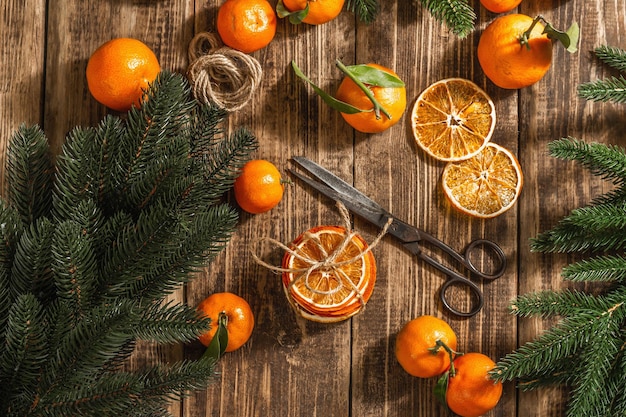 Dry oranges slices snack. Dried citrus fruits for Christmas decorations. Tangerines with leaves, fir tree branches, scissors, and thread. Wooden background, rustic concept, top view