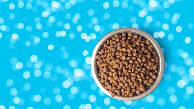 Dry pet food in a metal bowl isolated on blue background bokeh Food for cats and dogs pattern