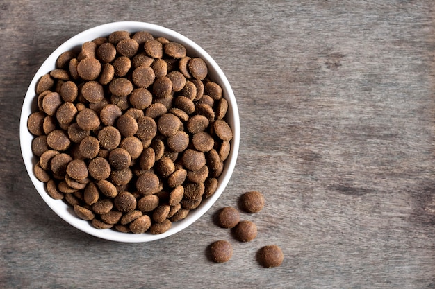 Dry pet food in a white ceramic bowl on wooden surface