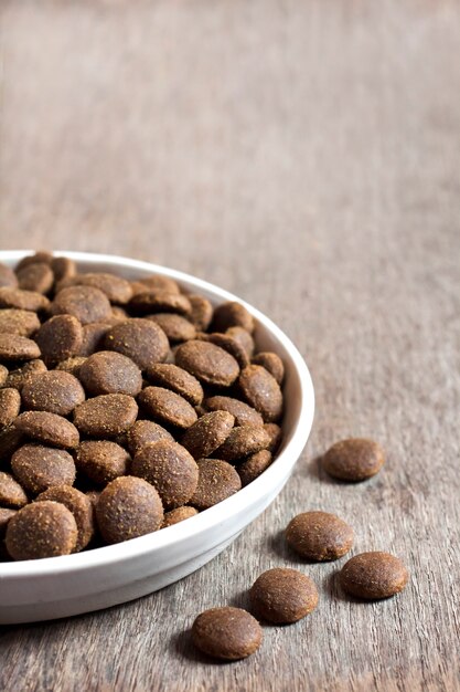 Dry pet food in a white ceramic bowl on wooden surface