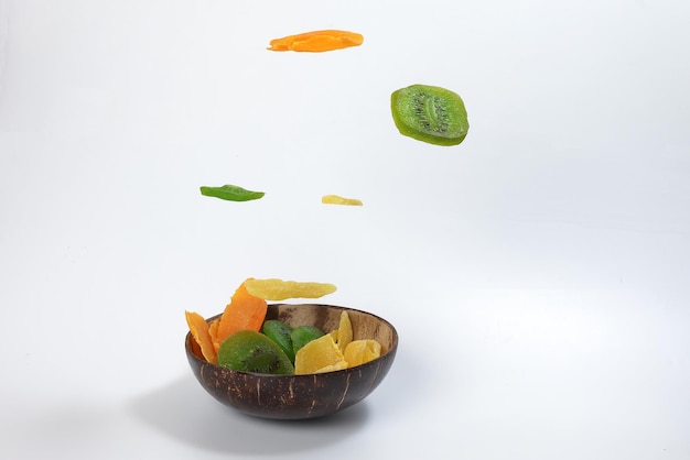 Dry preserved green kiwi pineapple ripe fruit slice colorful sweet on black marble slate background coconut shell bowl flying floating elevated drooping