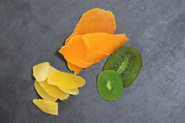 Dry preserved green kiwi pineapple ripe fruit slice colorful sweet on black marble slate background coconut shell bowl