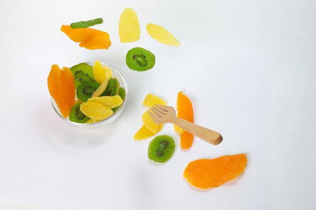 Dry preserved green kiwi pineapple ripe fruit slice colorful sweet on black marble slate background glass bowl flying floating elevated drooping