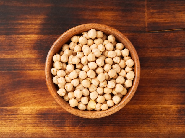 Dry raw chickpeas in wooden bowl on dark brown rustic background, top view