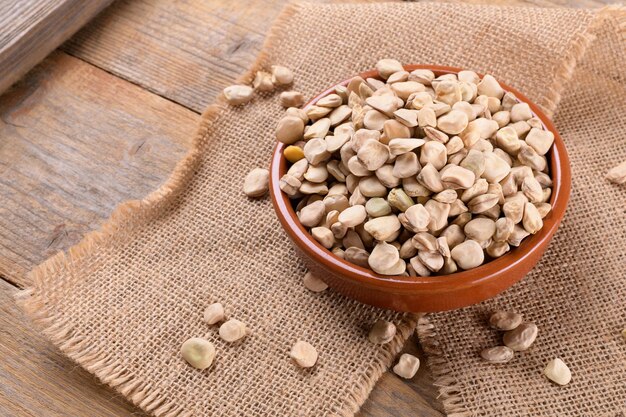 Photo dry raw cicerchia or indian pea on a clay plate with napkin on natural wooden background close up