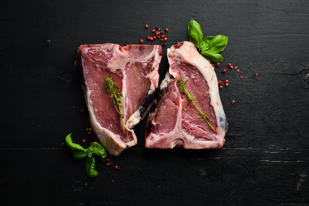 Dry raw two Tbone steak on the bone with spices on a black stone background Top view Rustic style