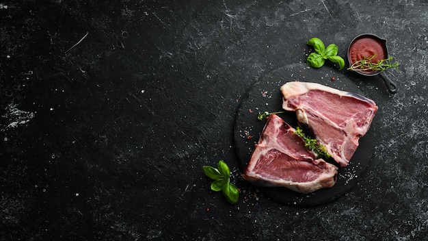 Dry raw two Tbone steak on the bone with spices on a black stone background Top view Rustic style