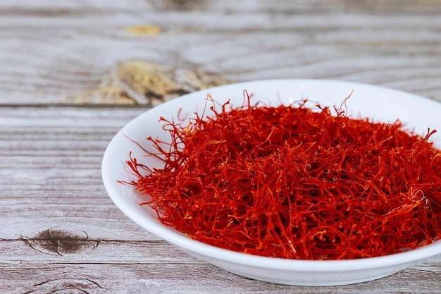 Dry red saffron stamens in a white plate on a wooden background. Saffron spice.