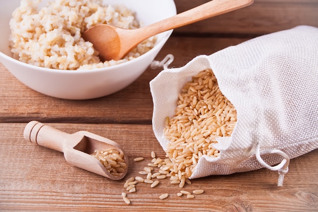 Dry rice in a bag and cooked brown rice in white bowl on wood