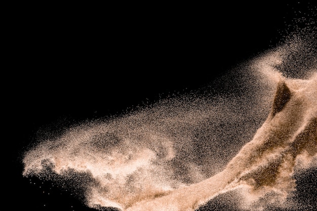 Dry river sand explosion. Golden colored sand splash agianst dark background.