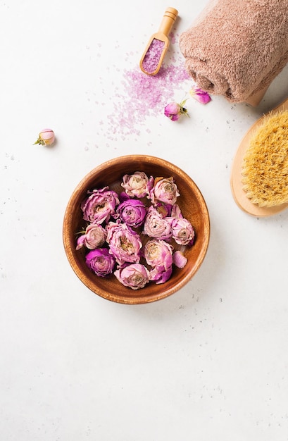 Dry rose flowers brush towel and pink salt Wellness spa and body care flat lay concept on white background copy space top view