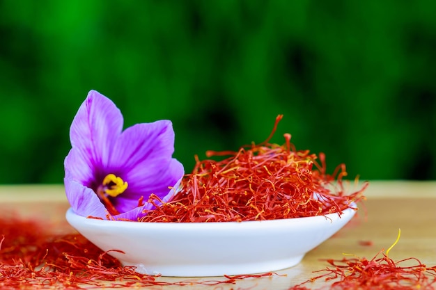 Foto stimmi di zafferano secco e un singolo fiore di croco in un piatto bianco su una superficie di legno spezie allo zafferano