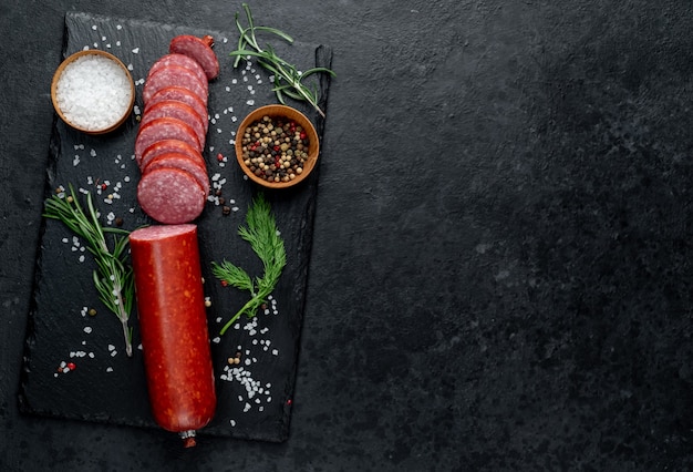 Dry salami sausage with fresh rosemary and spices on a stone background