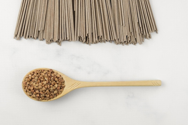 Pasta secca di grano saraceno soba e cucchiaio di legno con grano saraceno su un piano di lavoro in marmo bianco. cibo tradizionale giapponese, cibo asiatico e alimentazione sana. tipi alternativi di farine di cereali diversi.