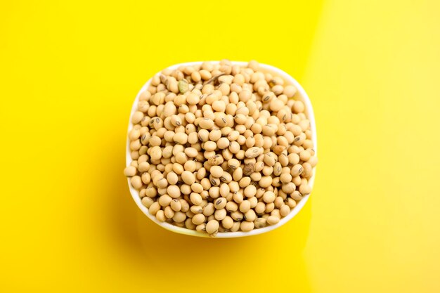 Dry soybean seed in bowl on yellow background