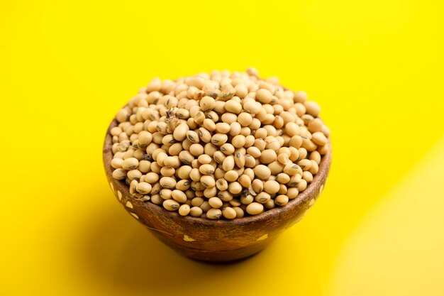 Dry soybean seed in wooden bowl on yellow background