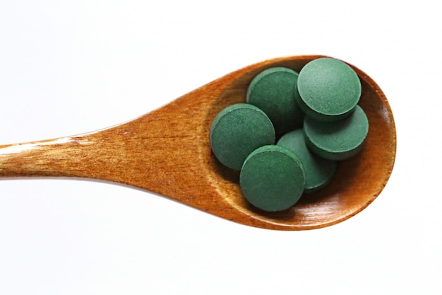 Dry spirulina in tablets in a wooden spoon