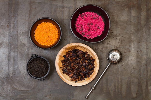 Dry tea in plates and bowls with a tea infuser on a metal table in a top view