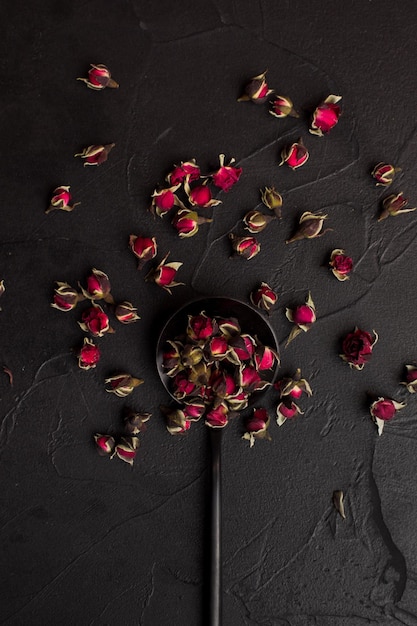 Dry tea rose buds on black spoon