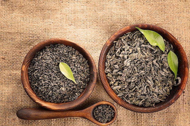 Dry tea with green leaves in wooden bowls on burlap background