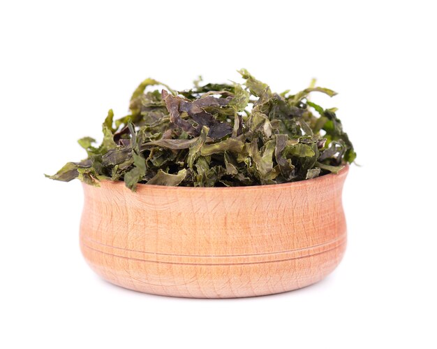 Dry wakame seaweed in wooden bowl, isolated on white. sea kale, asian dry food.