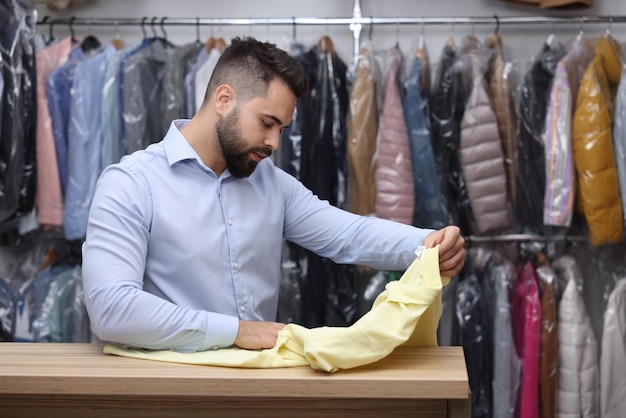 Drycleaning service Worker holding tshirt at counter indoors