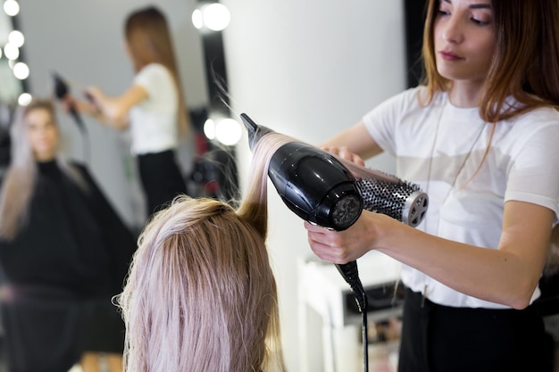 長いブロンドの髪をヘアドライヤーと丸いブラシで乾かします