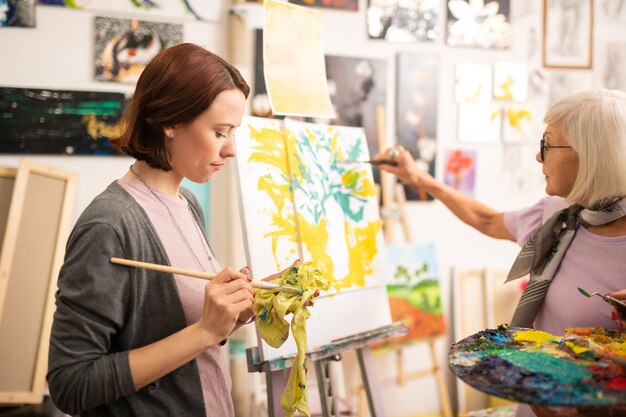 絵筆を乾かします。緑のガッシュの後に彼女の絵筆を乾かす黒髪の芸術学生