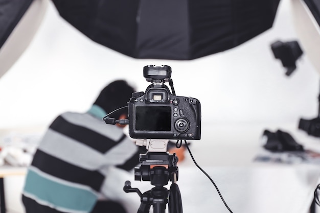 Камера DSLR и штатив в студии на фоне того, кто расставляет фотообъекты