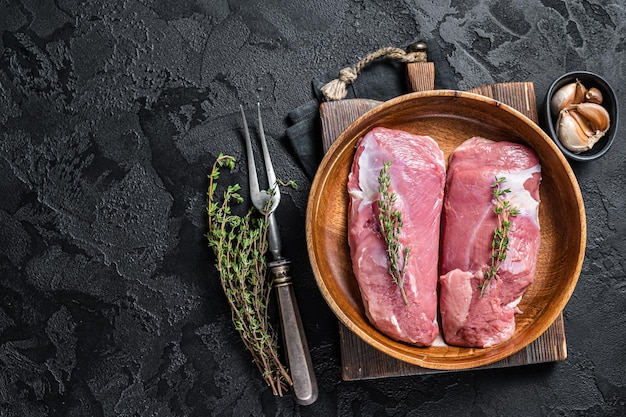 Duck breast fillet in wooden plate, raw poultry meat steaks. Black background. Top view. Copy space.