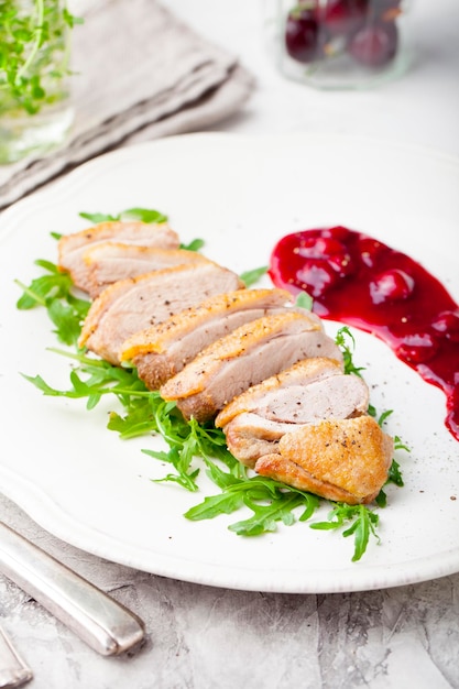 Duck breast meat with fresh salad arugula and cherry sauce on a white plate