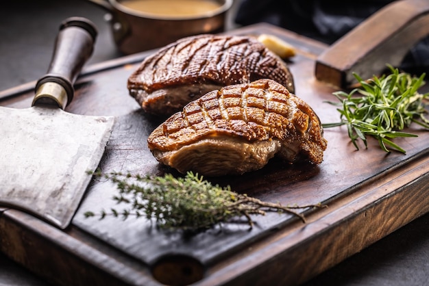 Duck breast with rosemary, thyme and butcher cleaver on a wooden tray.