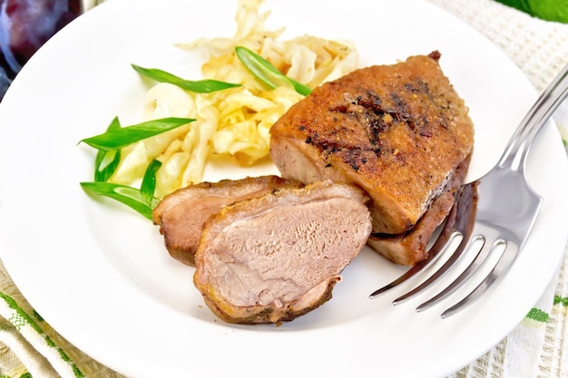 Duck breast with stewed cabbage and green onions in a white plate fruits sauce green towel on a wooden plank background