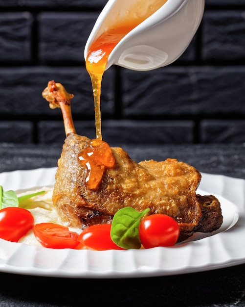 Duck confit with parsnip puree and orange sauce cherry tomatoes, fresh spinach served on a white plate with golden cutlery on a dark wooden background, top view, close-up