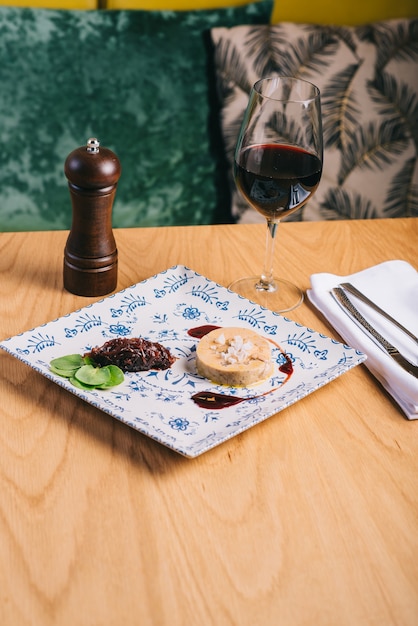 Duck foie gras with sauce on a wooden table and a glass of wine